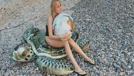 Alla blows off a beach ball while sitting on an inflatable turtle on the beach!!!
