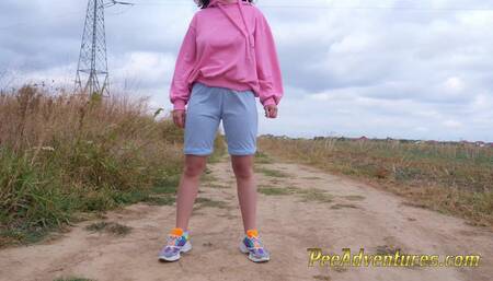 Hipster girl with a hoodie pee trough her jeans and pee next to the wheel of the car