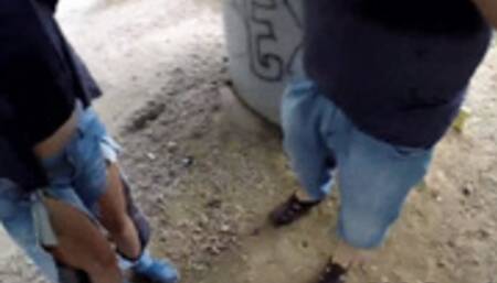 Under a bridge, a slutty brunette sucks two cocks