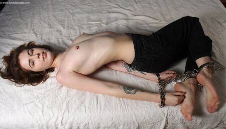 Rachel: topless barefoot girl, wearing only a black jeans, hogcuffed with steel cuffs, is wiggling on the bed, then is teased and tickled by camera man (HD MP4)