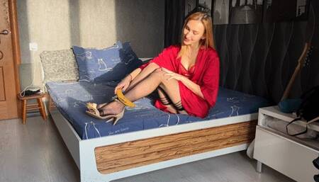 girl in high-heeled sandals plays with a banana, imagining it's a penis