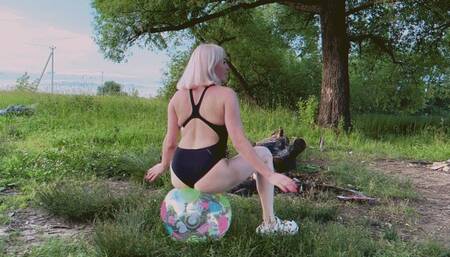 Alla pumps up a beach ball and jumps on it and it suddenly bursts