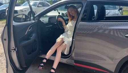 A girl in high-heeled shoes presses the pedals of her car and enjoys the sounds of the car engine