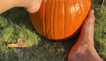 Tiippy is barefoot on the sidewalk stomping around and playing with a pumpkin with her feet