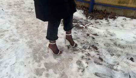 A girl in high-heeled shoes with open toes went out for a walk in winter, her heels are sliding on the ice and she is always slipping