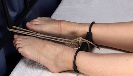 Topless tapegagged barefoot Alina, cuffed with strict handcuffs by hands and feet, stretched on the bed between headboard and footboard, is trying to ease her position (HD MP4)